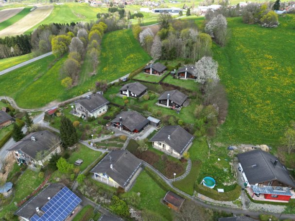 Luftaufnahme einer ländlichen Siedlung mit mehreren Einfamilienhäusern und grünen Wiesen.
