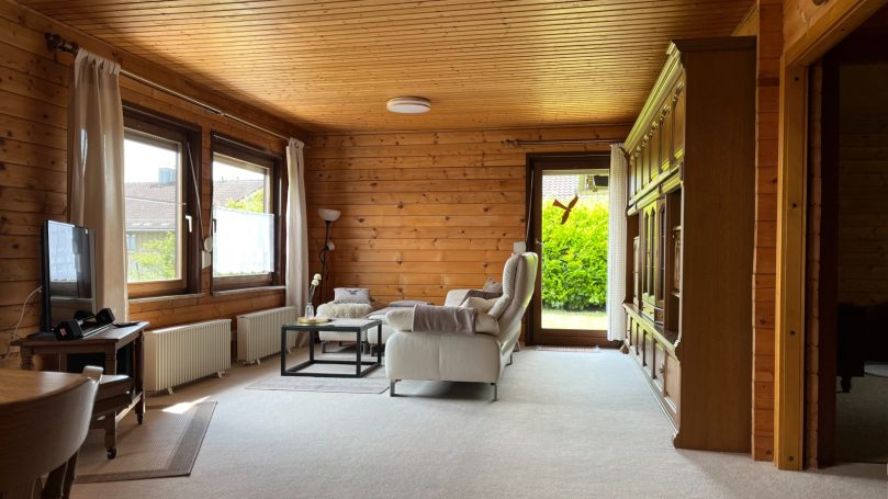 Helles Wohnzimmer mit Holzverkleidung und Zugang zu einem grünen Außenbereich.