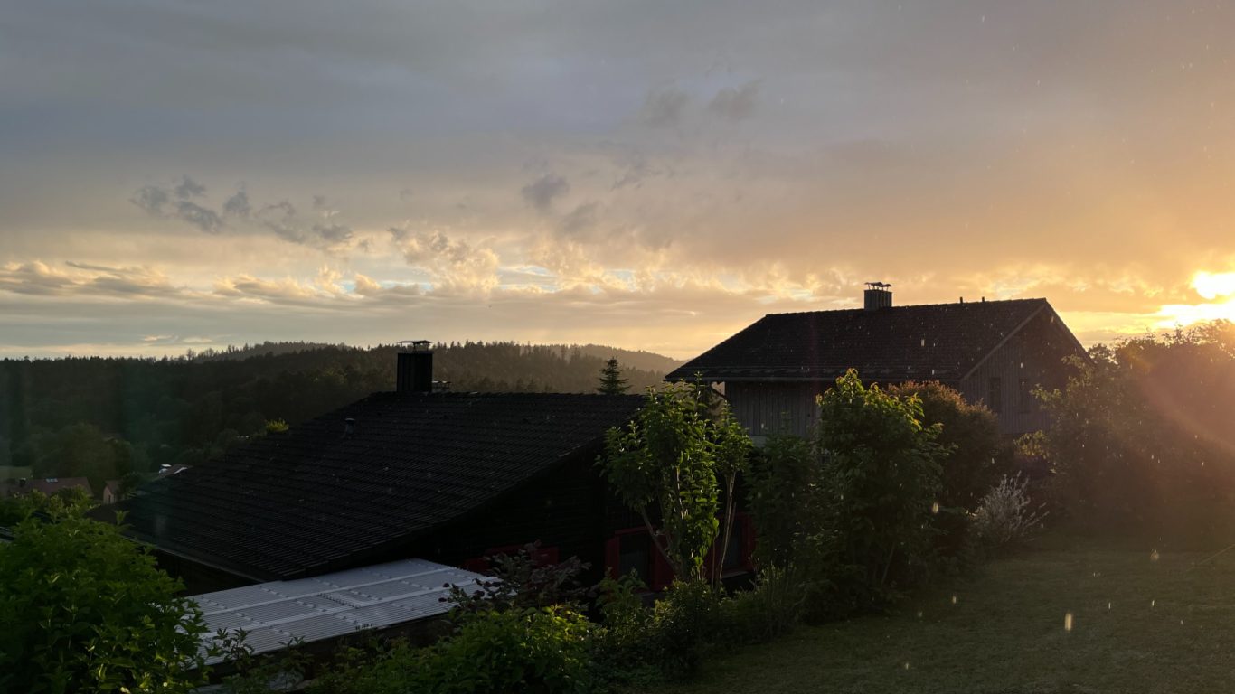 Sonnenuntergänge Sonnenuntergang über einem ländlichen Haus mit Bäumen im Vordergrund.