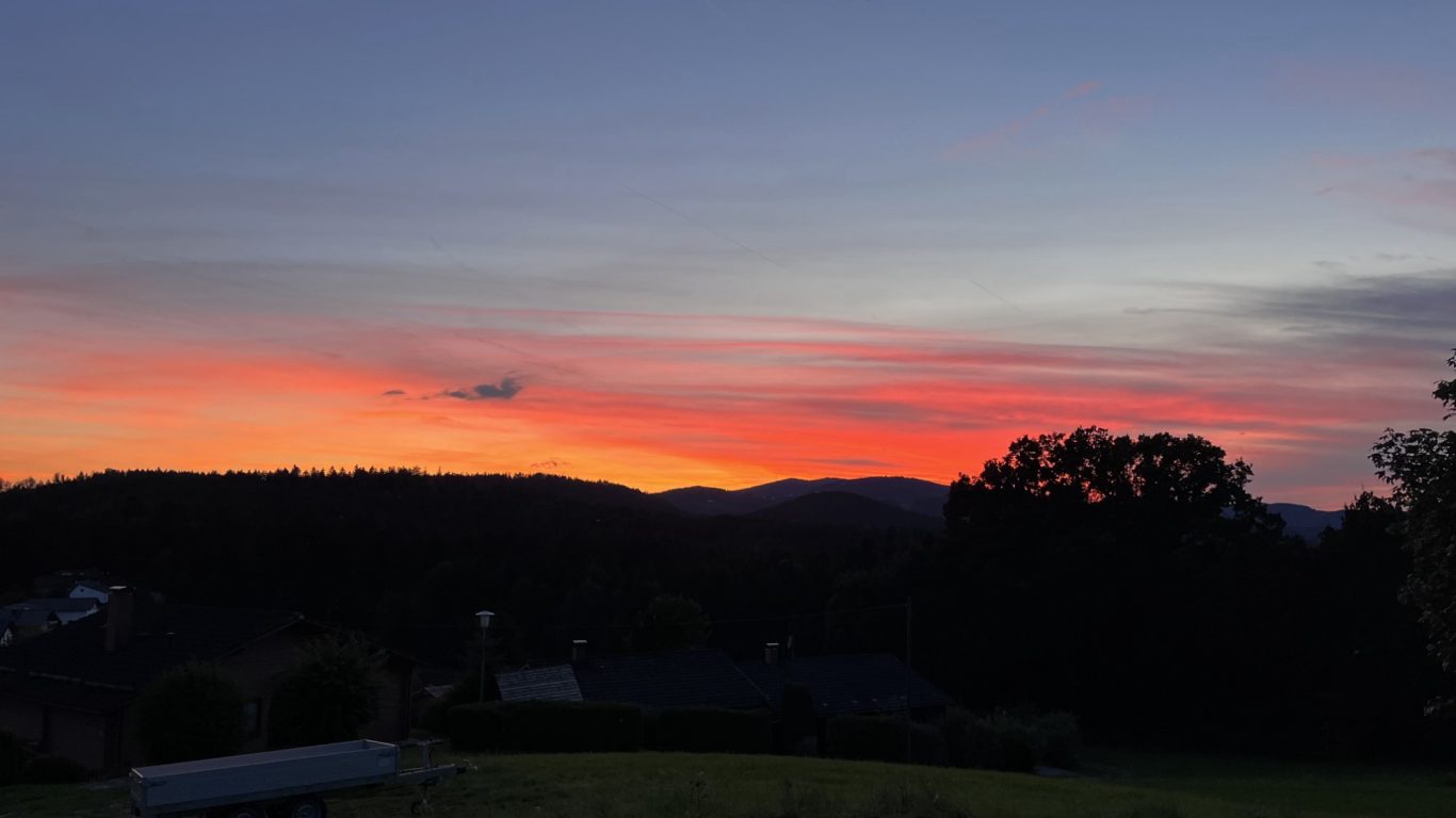 Abendrot Farbige Abenddämmerung über silhouettenhaften Bergen und Bäumen.