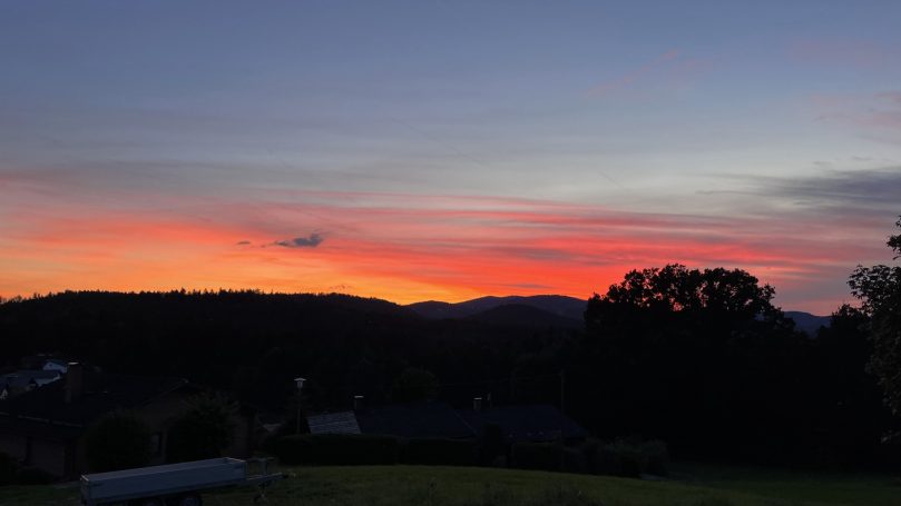 Farbige Abenddämmerung über silhouettenhaften Bergen und Bäumen.