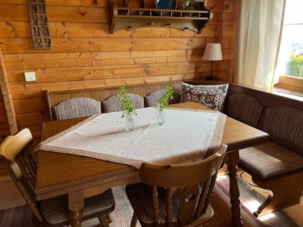 Holztisch in gemütlicher Stube, dekoriert mit einer Tischdecke und Pflanzen in Vasen.