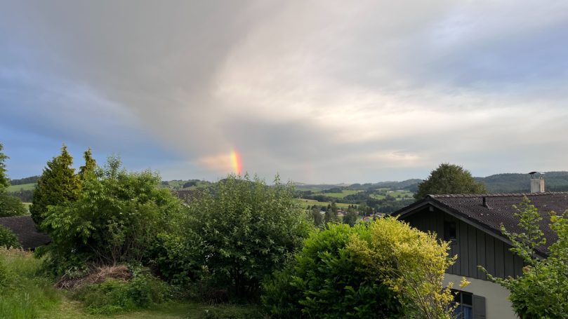Regenbogen über einer grünen Landschaft mit bewölktem Himmel.