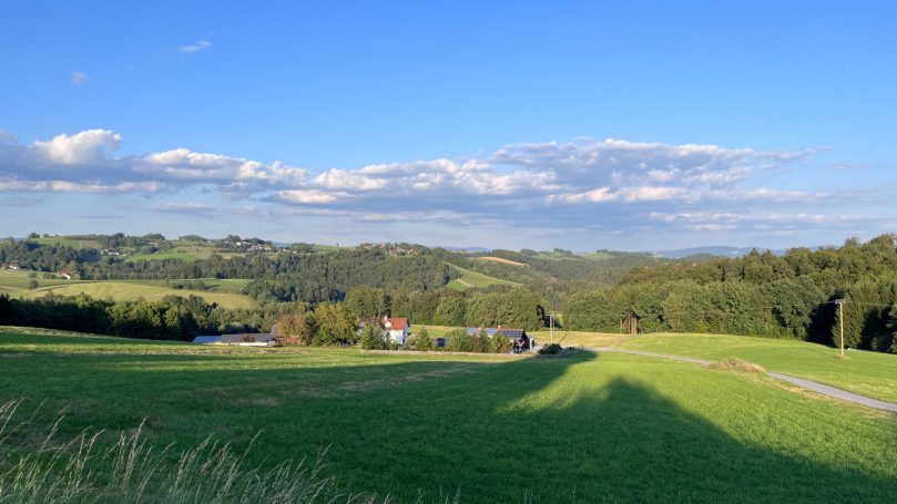 Landschaft mit Wiesen, Hügeln und einem klaren blauen Himmel.